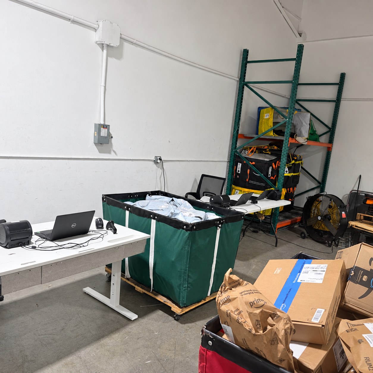 Packages in a rolling sorting bin beside a warehouse workstation and storage racks